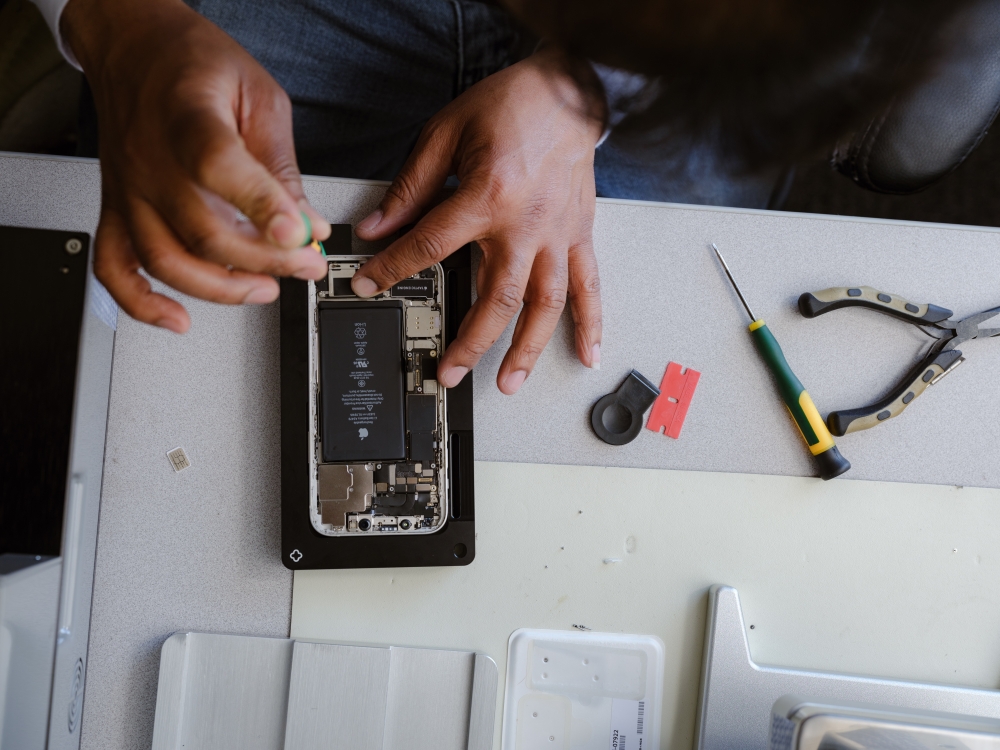 An independent repair technician, replacing the battery on an iPhone 12 using Apple’s certified repair equipment