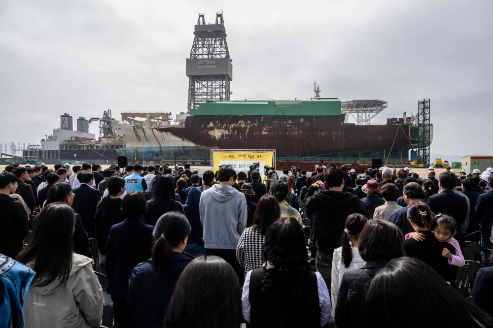 Guests bow their heads during a moment of silence during a remembrance ceremony in front of the salvaged Sewol ferry (back) at a port in Mokpo, South Jeolla Province, on April 16, 2024, as South Korea marked the 10th anniversary of the country's worst-ever maritime disaster, when hundreds of schoolchildren died after the overloaded Sewol ferry capsized and sank.  (Photo by ANTHONY WALLACE / AFP)