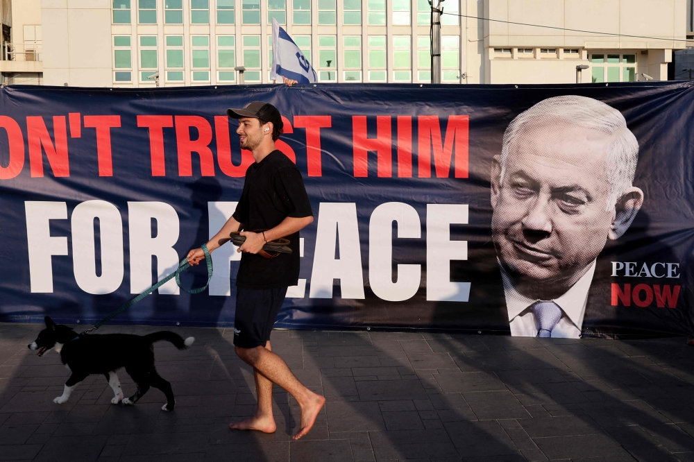 A man walks his dog next to a banner during a protest in front of the US Embassy branch office in Tel Aviv. — AFP 