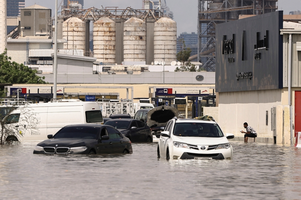 A person sits near vehicles stranded in flood water caused by heavy rains in Dubai, United Arab Emirates, April 17, 2024. REUTERS/Amr Alfiky