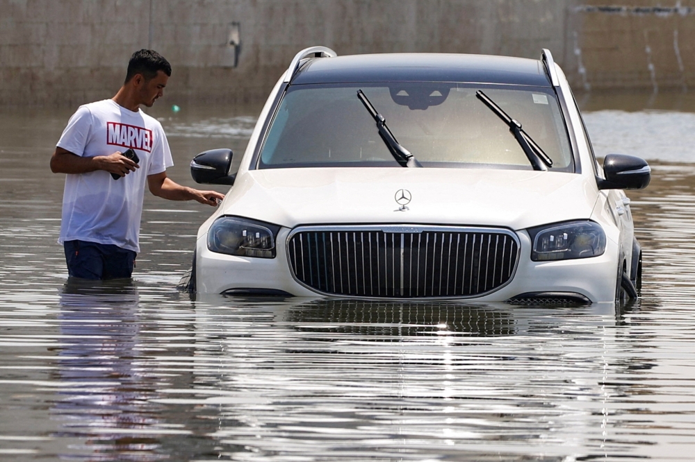 A man stands next to a car partially submerged by flood water following heavy rainfall