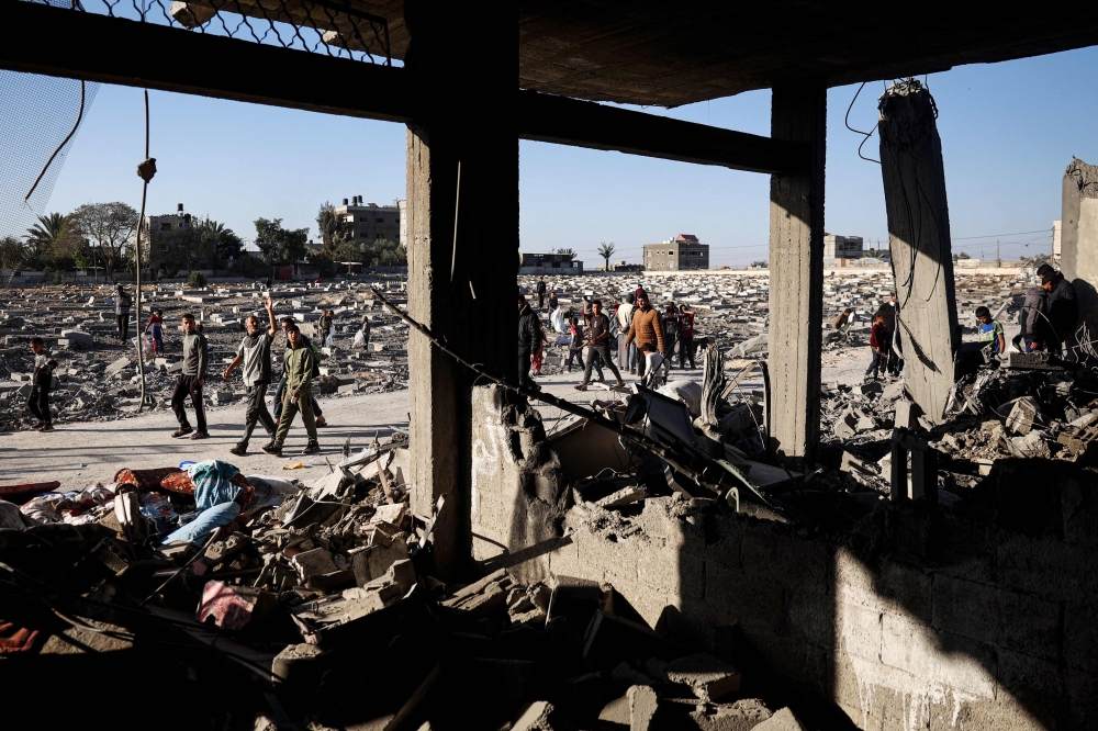 Palestinians walk between a cemetary and a building hit by overnight Israeli bombing in Rafah in the southern Gaza Strip. — AFP 