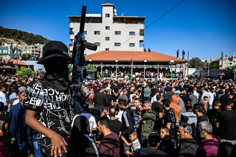 An armed and masked youth takes part in the funeral procession of Palestinians killed in an Israeli raid in the Nur Shams camp for Palestinian refugees in the occupied West Bank, on April 21, 2024.  The Israeli army said it killed 10 militants during the operation in the camp, which started on April 18. (Photo by RONALDO SCHEMIDT / AFP)