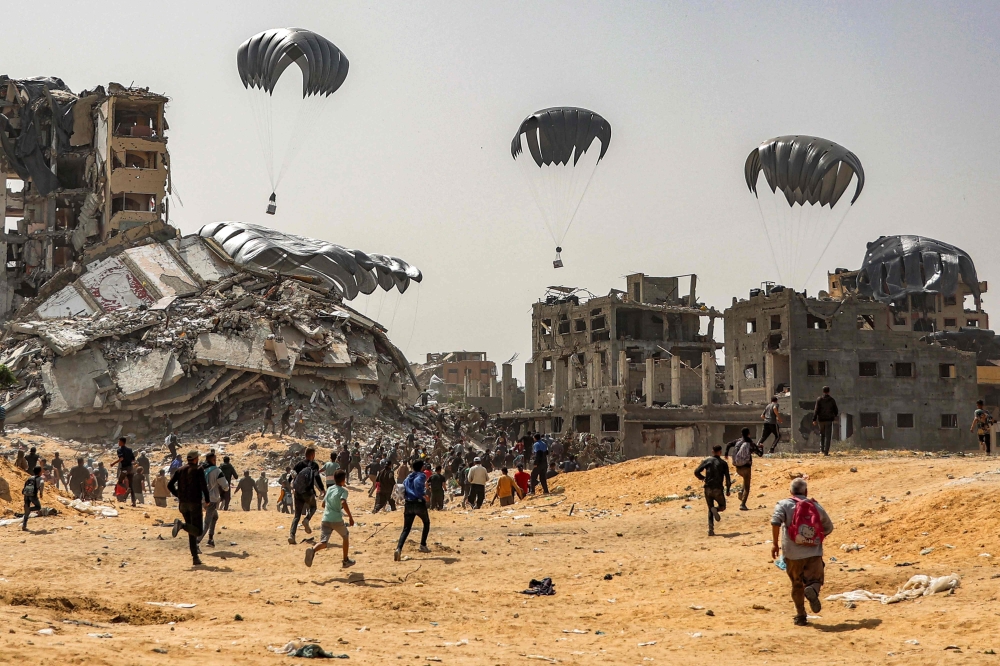 People rush to landing humanitarian aid packages dropped over the northern Gaza Strip. — AFP 