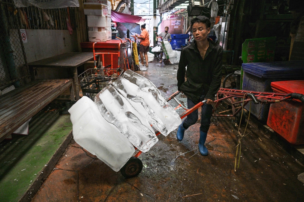 A worker transports blocks of ice through a fresh market on a hot day in Bangkok 