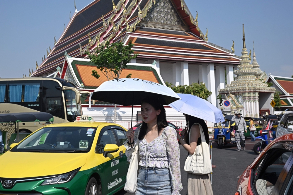 Tourists shield themselves from the sun with umbrellas to combat the heat outside Wat Pho Buddhist temple in Bangkok 