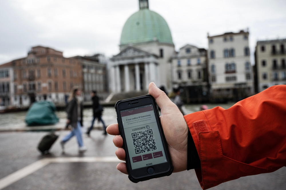 A phone shows a QR code to access the city displayed on a smart phone in front of the Santa Lucia railway station as people wait to buy tickets in Venice on Thursday. — AFP