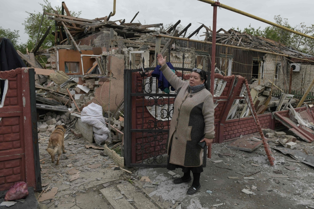 A woman gestures before a damaged apartment hit by recent shelling