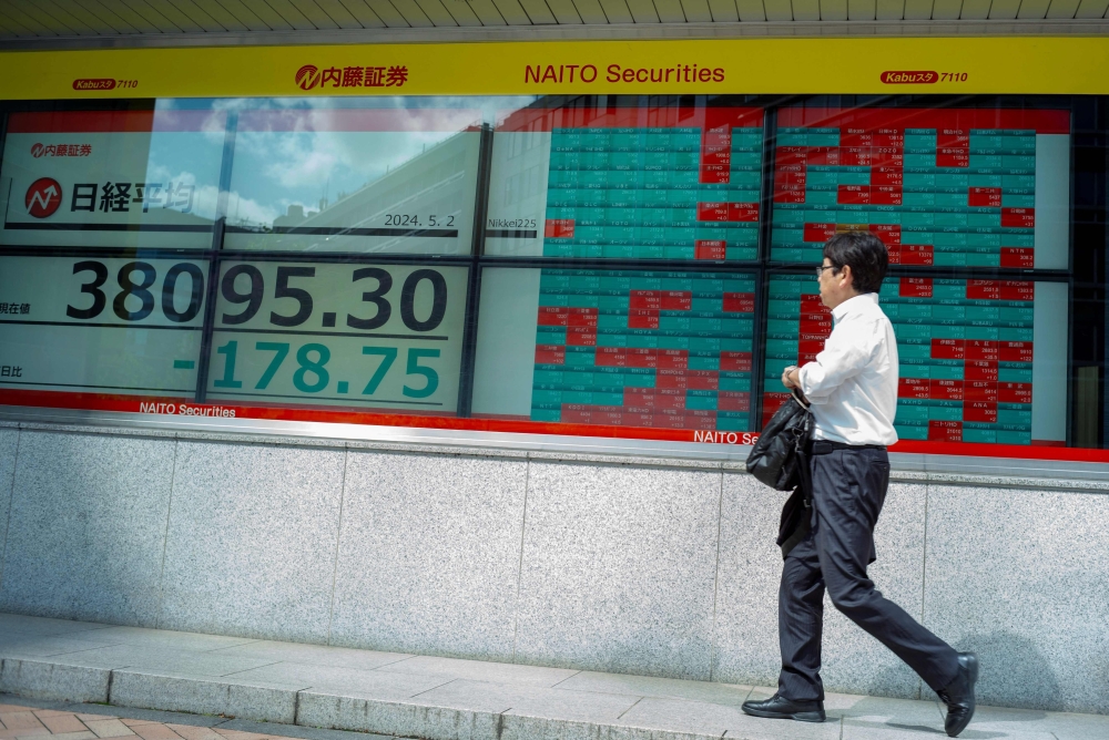  Aman walks in front of an electronic board displaying a share price of the Nikkei index of the Tokyo Stock Exchange along a street in Tokyo__AFP