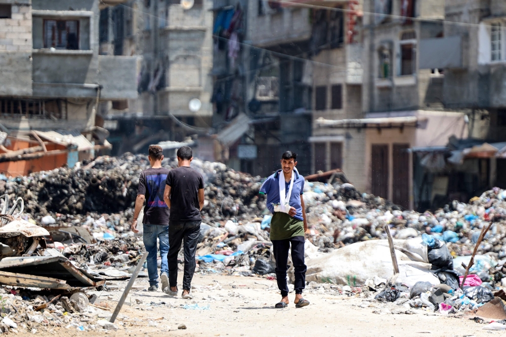 An injured Palestinian man walks near a rubbish dump in Gaza City 
