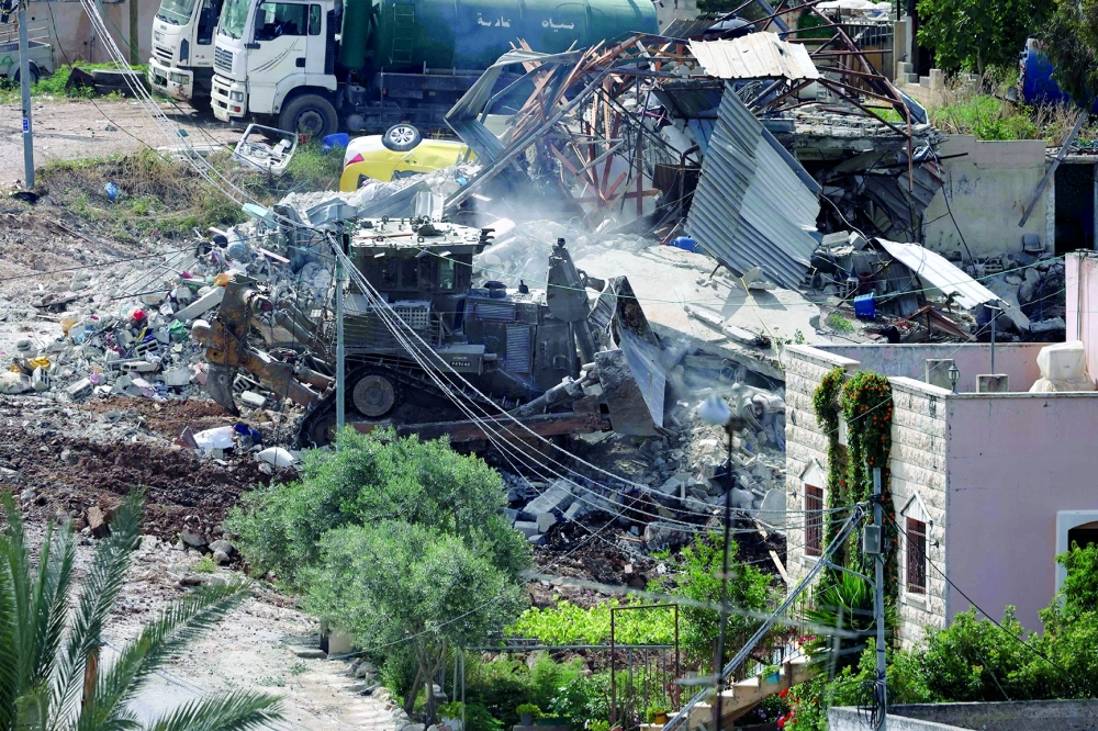 An Israeli army bulldozer operates amid the rubble of a demolished building during a raid in the West Bank. — AFP 