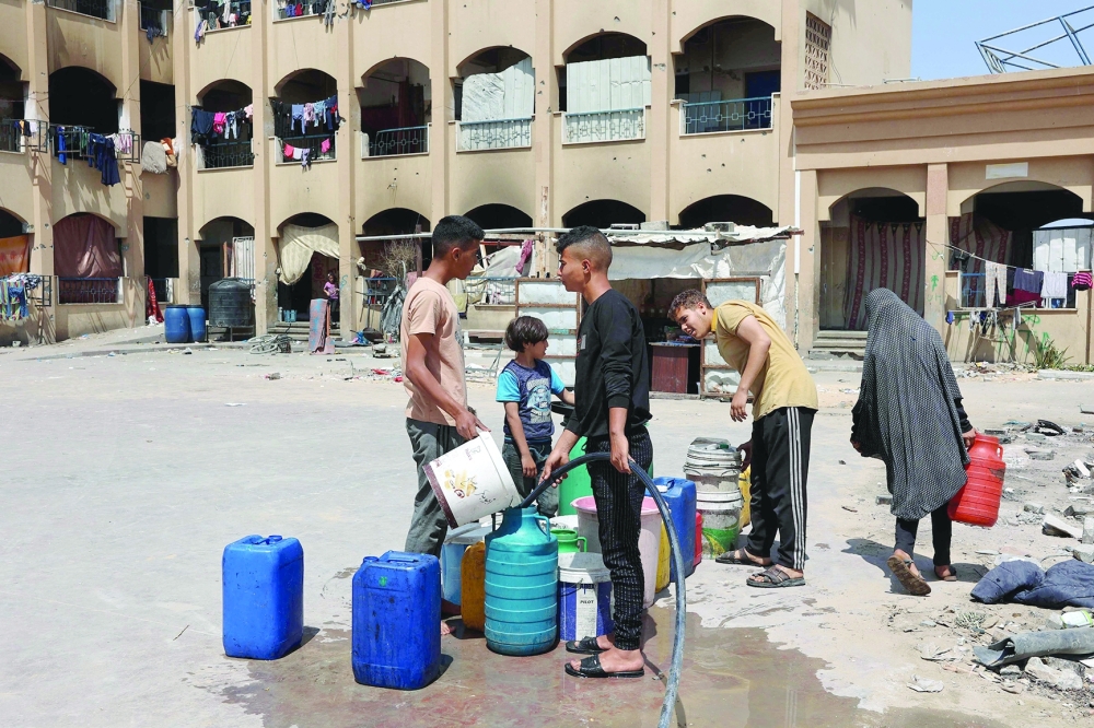 Displaced Palestinians fill jerrycans with water in a school used as a temporary shelter, in Beit Lahya. — AFP 