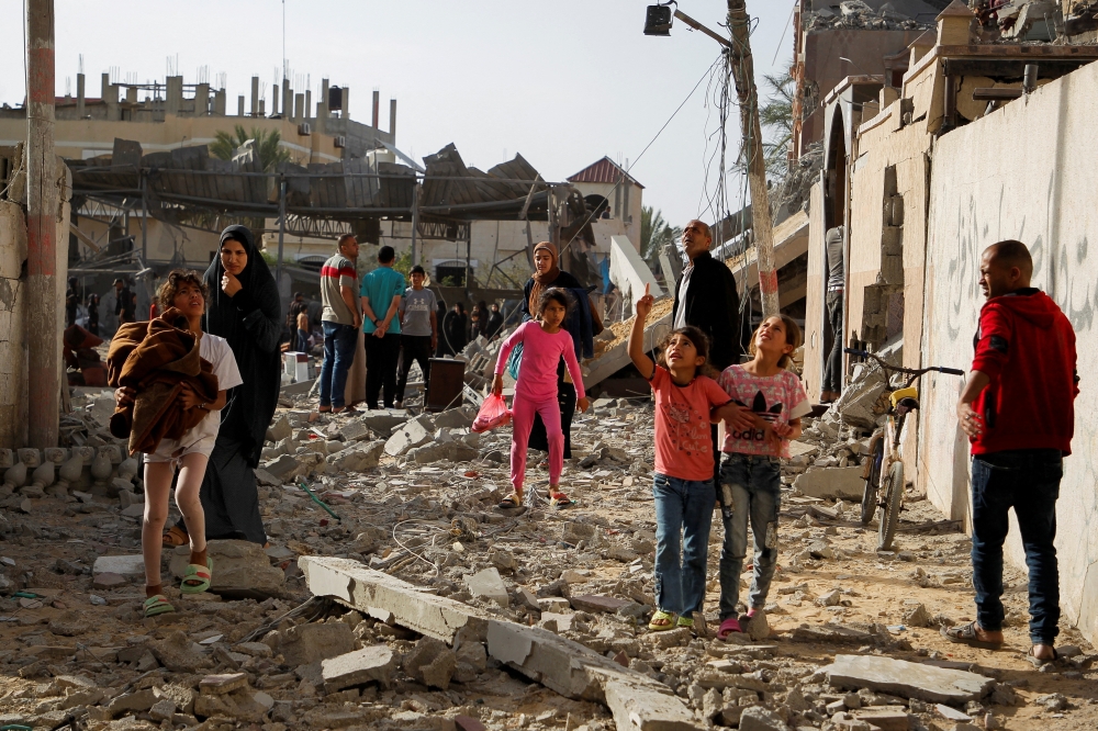 Palestinian children look up as they walk at the site of an Israeli strike on a house, in Rafah. — Reuters 