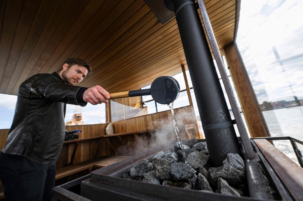 Architect Johan Strandlund pours water on a custom-made wood stove with hot rocks inside the "Big Branzino", a luxe floating sauna measuring 30 square metres, as it floats in the waters of the Swedish capital, Stockholm, on May 5, 2023. In Sweden and Finland, some unusual saunas have been built in recent years, offering truly singular experiences. - TO GO WITH AFP STORY by Viken KANTARCI
 (Photo by Jonathan NACKSTRAND / AFP) / TO GO WITH AFP STORY by Viken KANTARCI

