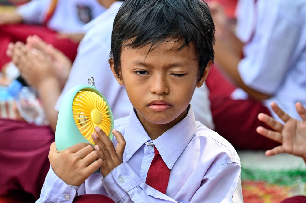 A student uses a portable fan to keep cool while studying outside the classroom 