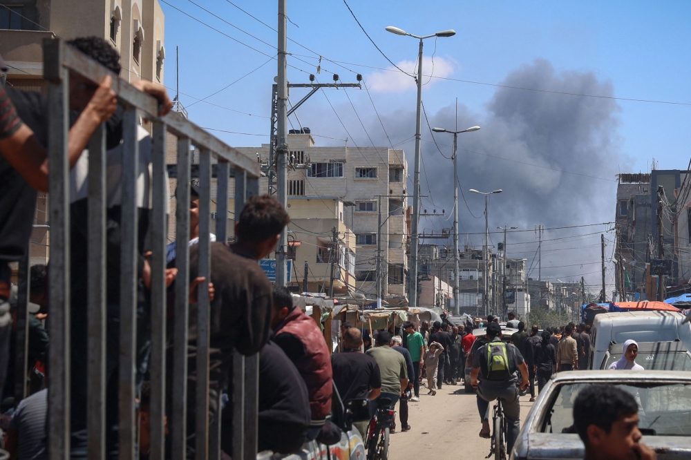 Palestinians crowd a street as smoke billows nearby from Israeli strikes in Rafah 