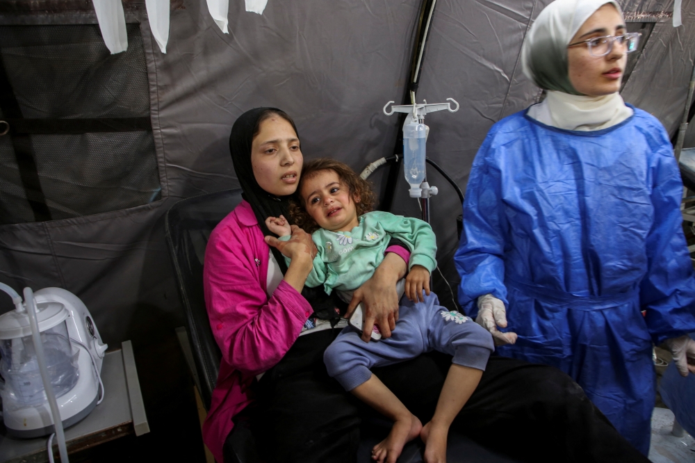A Palestinian woman holds a girl wounded in an Israeli strike, at a hospital 