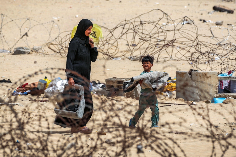A woman and boy walk with belongings past barbed-wire fences as they flee from Rafah. — AFP 