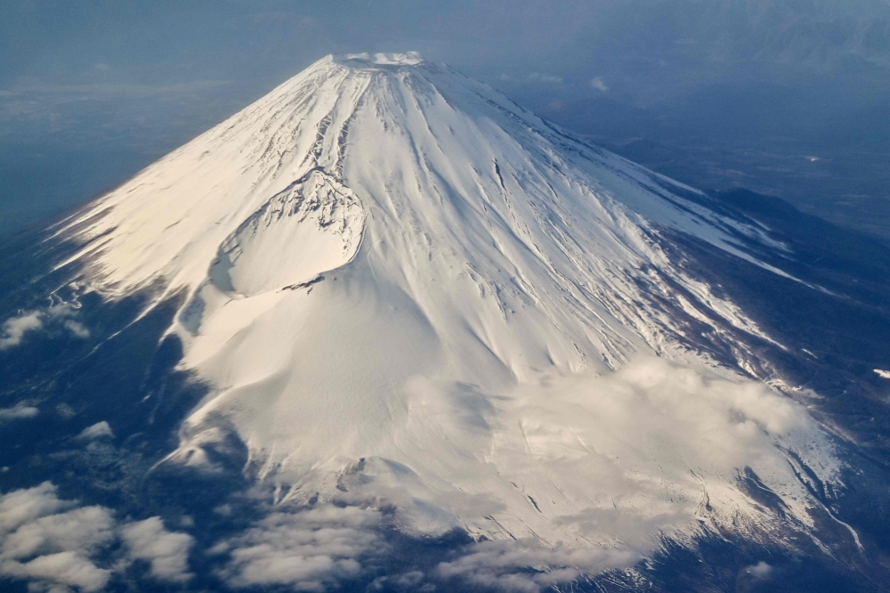 This photo taken on January 30, 2024 shows an aerial view of Mount Fuji, Japan's highest mountain at 3,776 meters (12,389 feet), from the window of a passenger jet. An online booking system for Mount Fuji's most popular trail was announced on May 13, 2024 by Japanese authorities trying to fight overtourism on the active volcano. (Photo by Richard A. Brooks / AFP)

