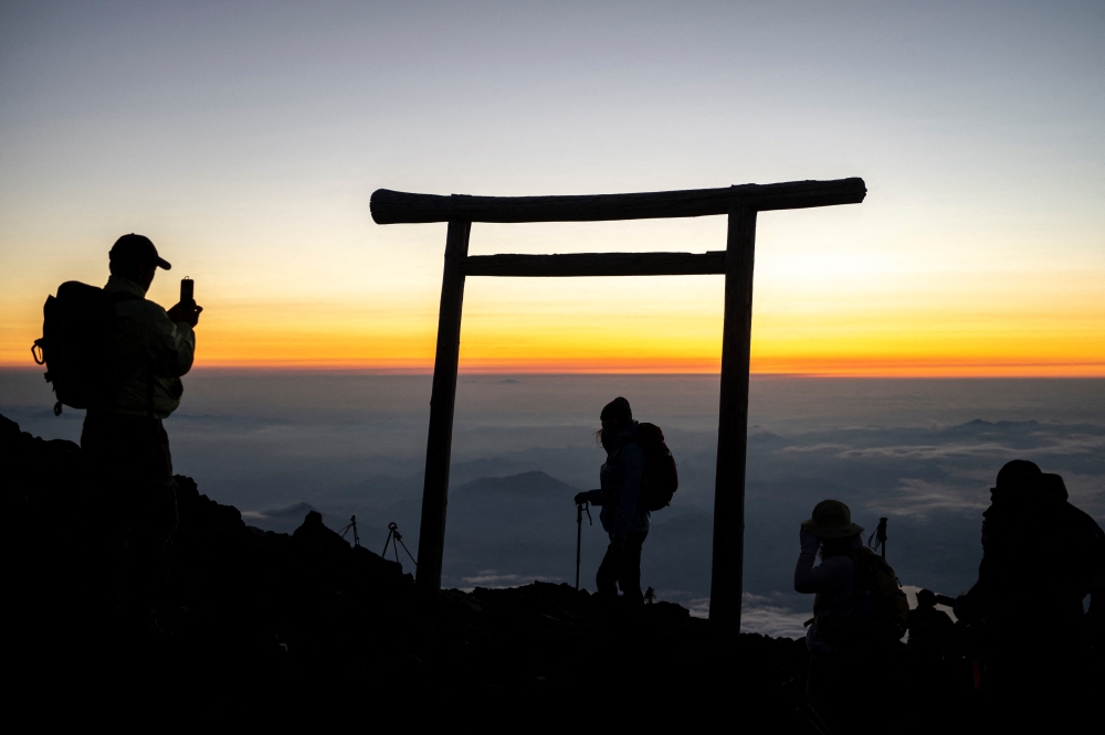 (FILES) This file photo taken on July 19, 2021 shows people watching the sunrise from the summit of Mount Fuji, some 70 kilometres (43 miles) west of the capital Tokyo. An online booking system for Mount Fuji's most popular trail was announced on May 13, 2024 by Japanese authorities trying to fight overtourism on the active volcano. (Photo by Charly TRIBALLEAU / AFP)

