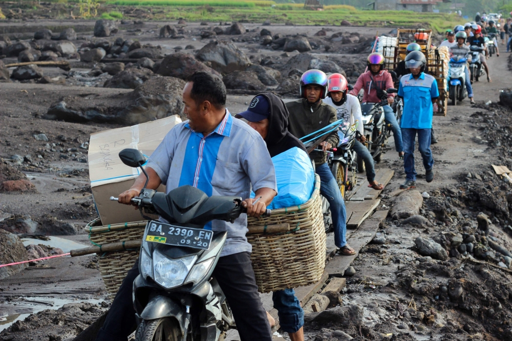 TOPSHOT - People drive their motorcycles over a makeshift pathway made from wodden slabs to avoid the mud that was caused by flash floods at Rambatan Village, Tanah Datar Regency, West Sumatra, on May 14, 2024. Rescuers recovered more bodies on May 14 after flash floods and cold lava flow on Indonesia's Sumatra island over the weekend killed at least 50 people and left another 27 missing, the country's disaster agency said.
 (Photo by ADE YUANDHA / AFP)