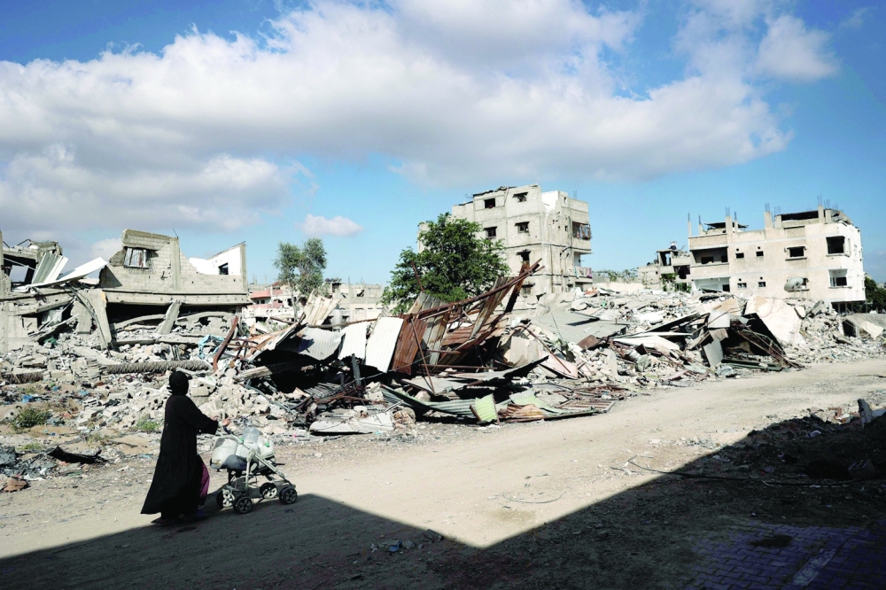 A displaced Palestinian woman pushes a stroller as she walks in front of destroyed buildings in Khan Yunis
