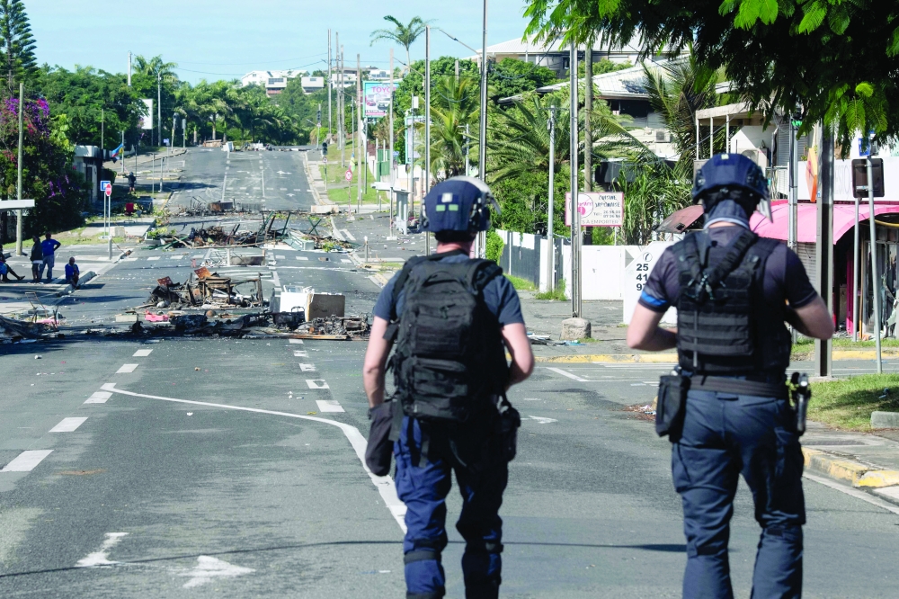 Police patrol a street blocked by debris and burnt out items following overnight unrest in the Magenta district of Noumea. — AFP 