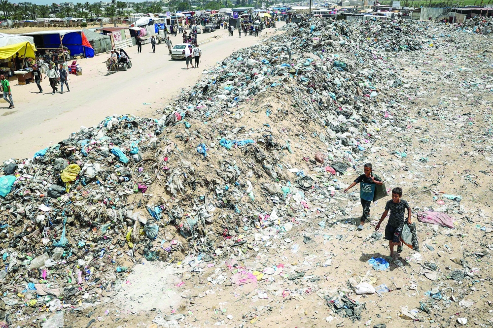 Children walk with bags of objects found in garbage piled up near tents set up by displaced Palestinians in Khan Yunis. — AFP 
