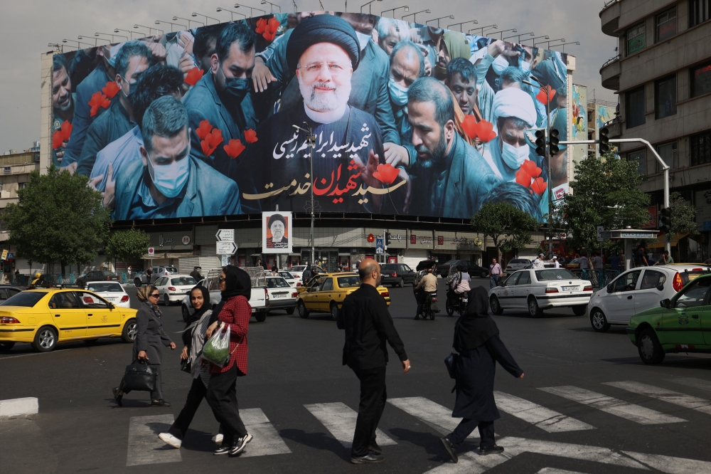 People walk past a billboard with a picture of the late Iran's President Ebrahim Raisi on a street in Tehran, Iran May 21, 2024.