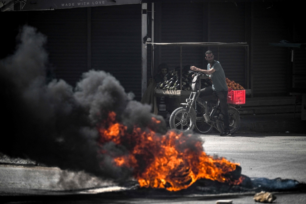 Palestinians look on behind burning tyres during an Israeli raid in the occupied West Bank city of Jenin. — AFP 