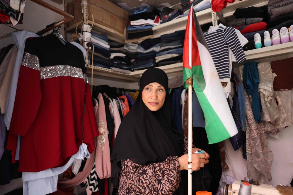 A shop owner carries a Palestinian flag in her store in the Palestinian refugee camp of Shatila in Beirut's southern suburb on May 22, 2024. Ireland, Norway and Spain said they would formally recognise the State of Palestine on May 28, drawing praises from  Palestinian leaders as well as many countries in the Arab and Muslim world, and fury from Israel. (Photo by ANWAR AMRO / AFP)
