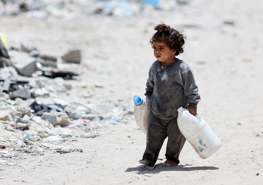 A Palestinian girl carries cans to collect water as she walks by houses which were destroyed in an Israeli strike, amid the ongoing conflict between Israel and Hamas, in Khan Younis, in the southern Gaza Strip, May 22, 2024. REUTERS/Mohammed Salem