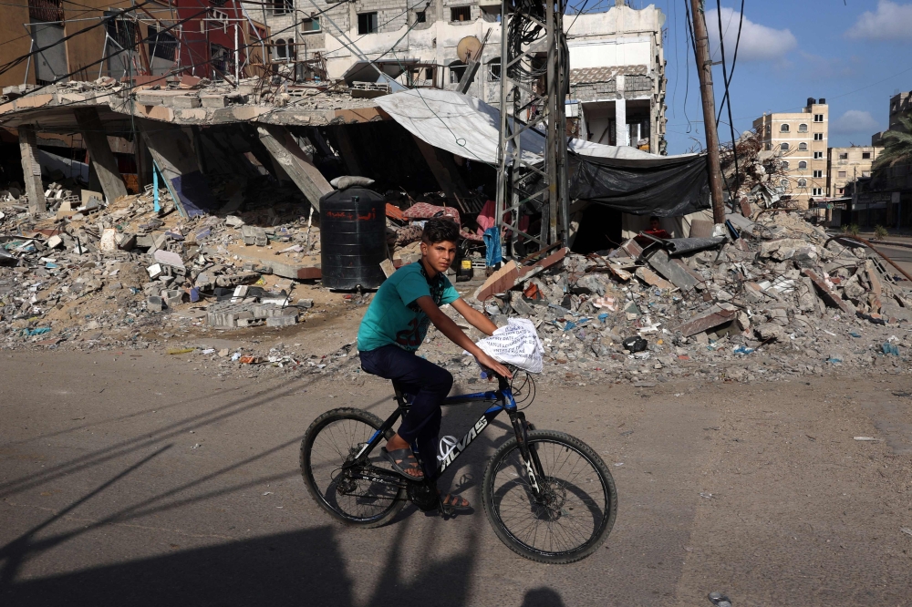 A Palestinian boy rides a bicycle past a destroyed building in Rafah in the southern Gaza Strip on Sunday. - AFP

