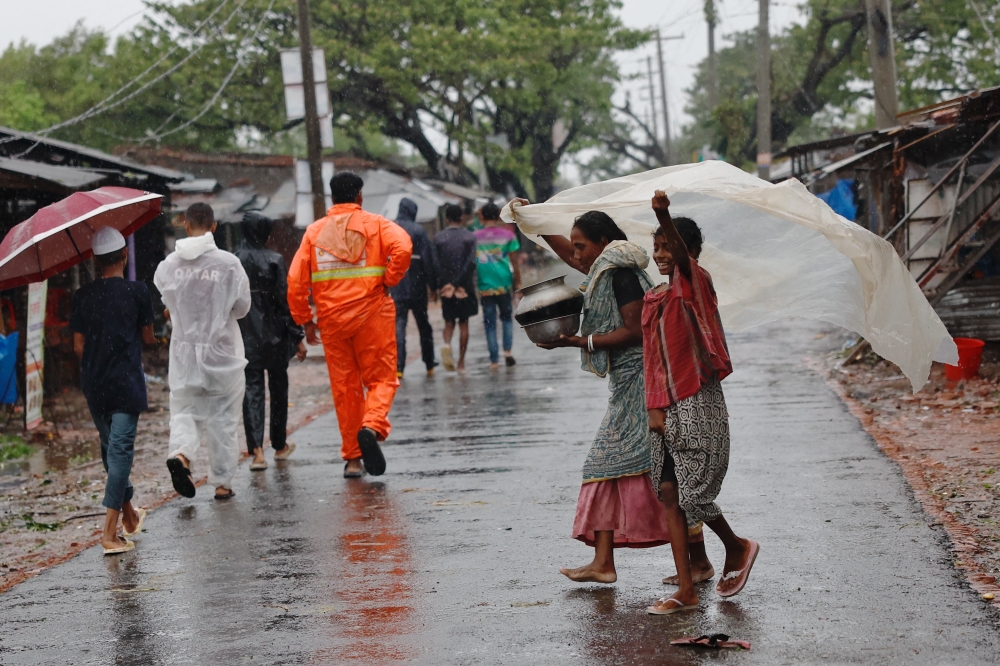 Women hold a polythene sheet to take cover from rain, as Cyclone Remal hits the country, in the Shyamnagar area of Satkhira, Bangladesh