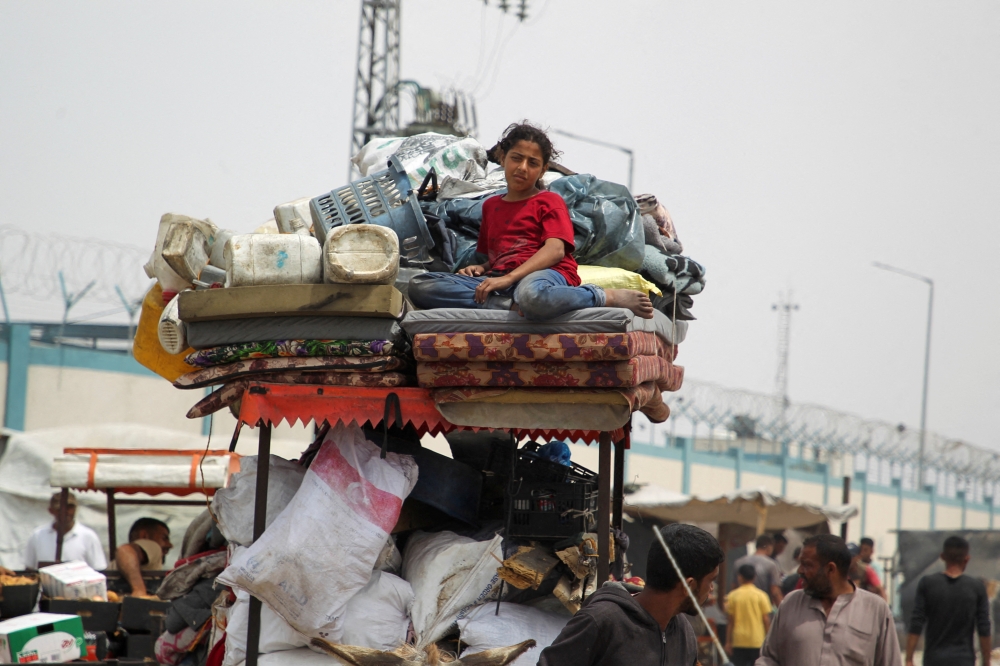 A girl looks on, while Palestinians travel with their belongings, as they flee Rafah due to an Israeli strikes. — Reuters 