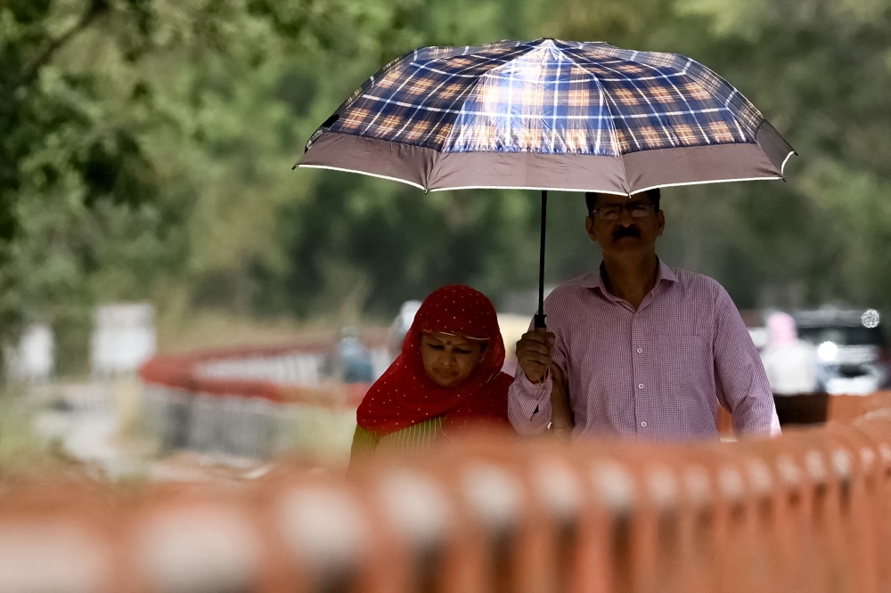 People walk under a umbrella on a hot summer afternoon in New Delhi on May 29, 2024, amid ongoing heatwave. Temperatures in India's capital have soared to a record-high 49.9 degrees Celsius (121.8 degrees Fahrenheit) as authorities warn of water shortages in the sprawling mega-city. (Photo by Arun SANKAR / AFP)
