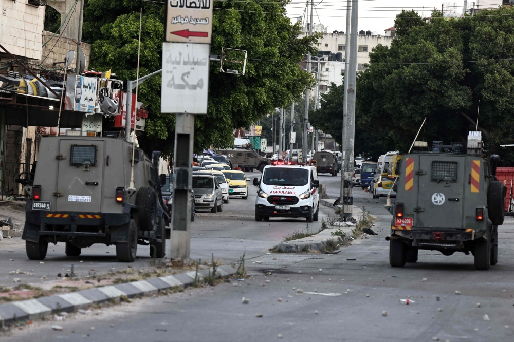 Israeli military vehicles drive by an ambulance during a raid in the Balata refugee camp in the occupied West Bank. — AFP 