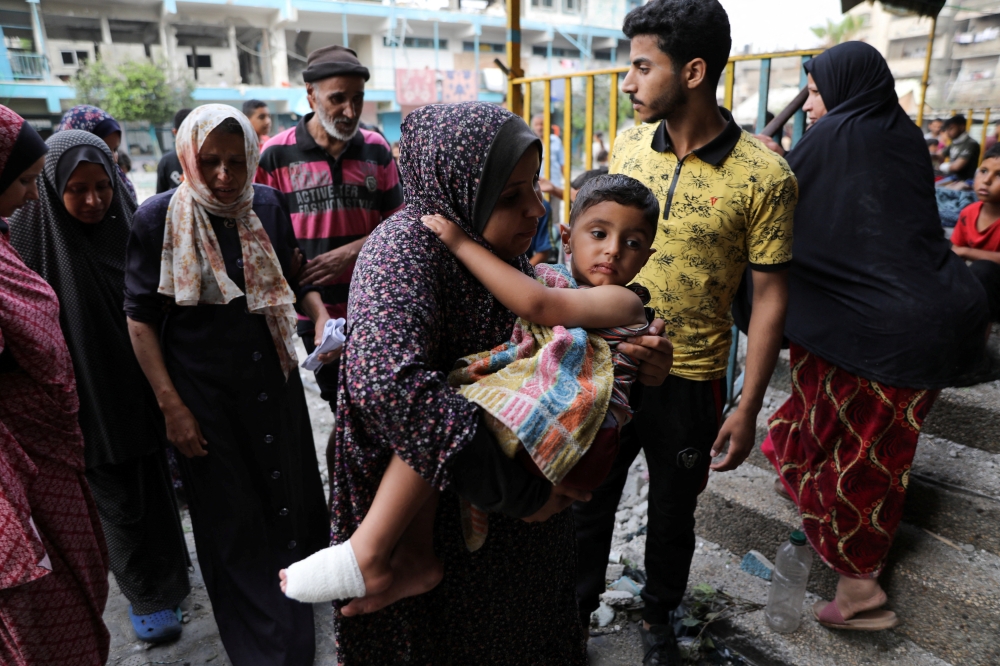 A woman carries a child at the site of an Israeli strike on a UNRWA school sheltering displaced people in Nuseirat refugee camp in the central Gaza Strip. - Reuters
