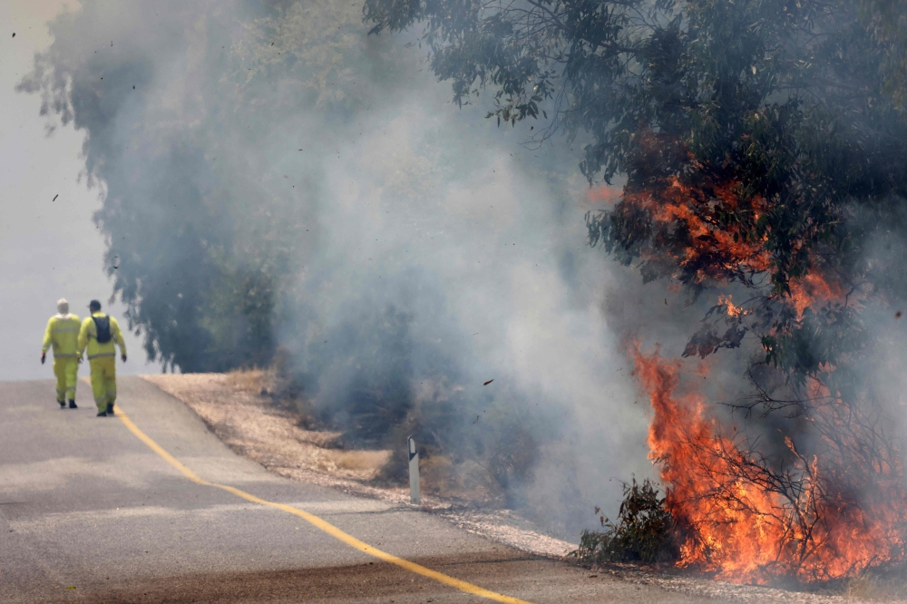 Israeli firefighters put out flames in a field after rockets launched from southern Lebanon landed on Banias area in the Golan Heights. — AFP 
