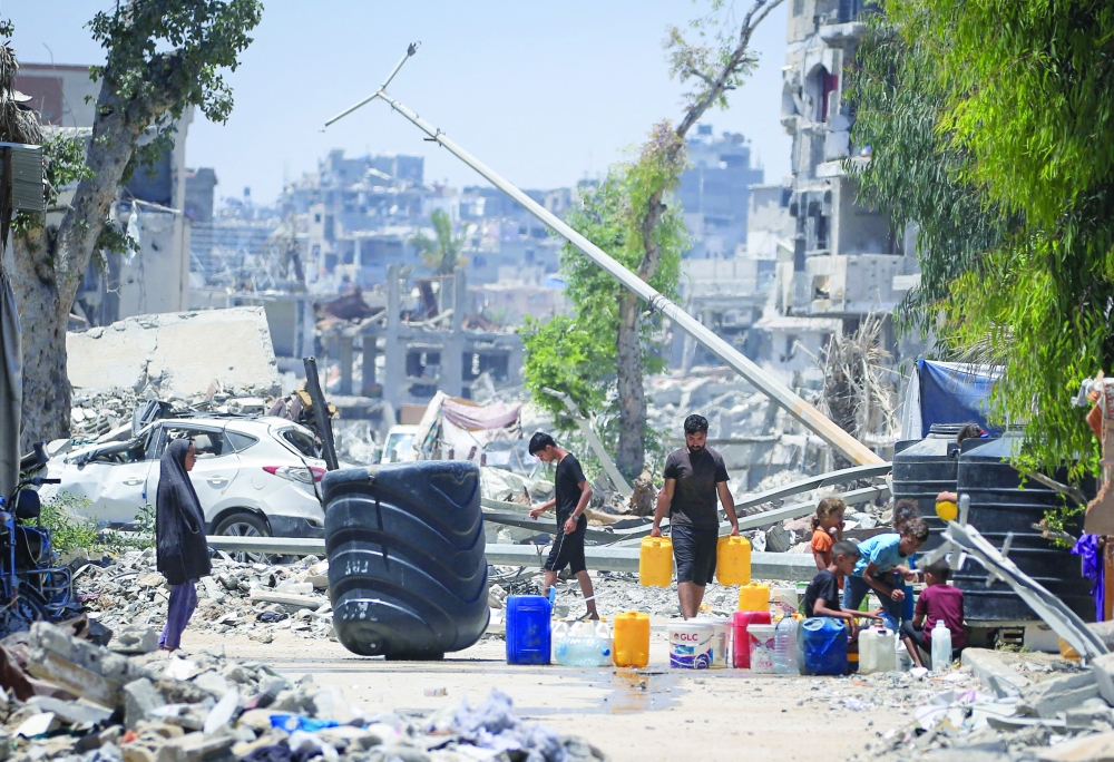 Palestinians collect water near buildings destroyed in the Israeli bombardment of Khan Yunis. — AFP 