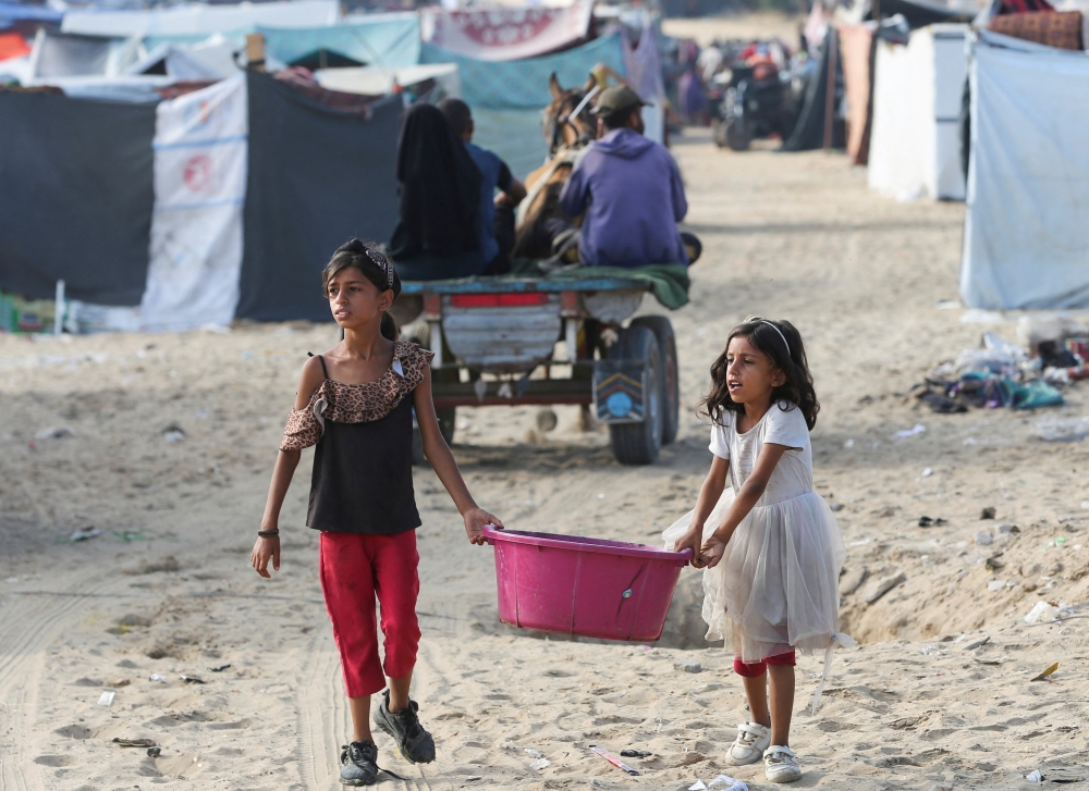 Girls walk carrying a container as Palestinians flee Rafah due to an Israeli military operation in Rafah on Thursday. — Reuters