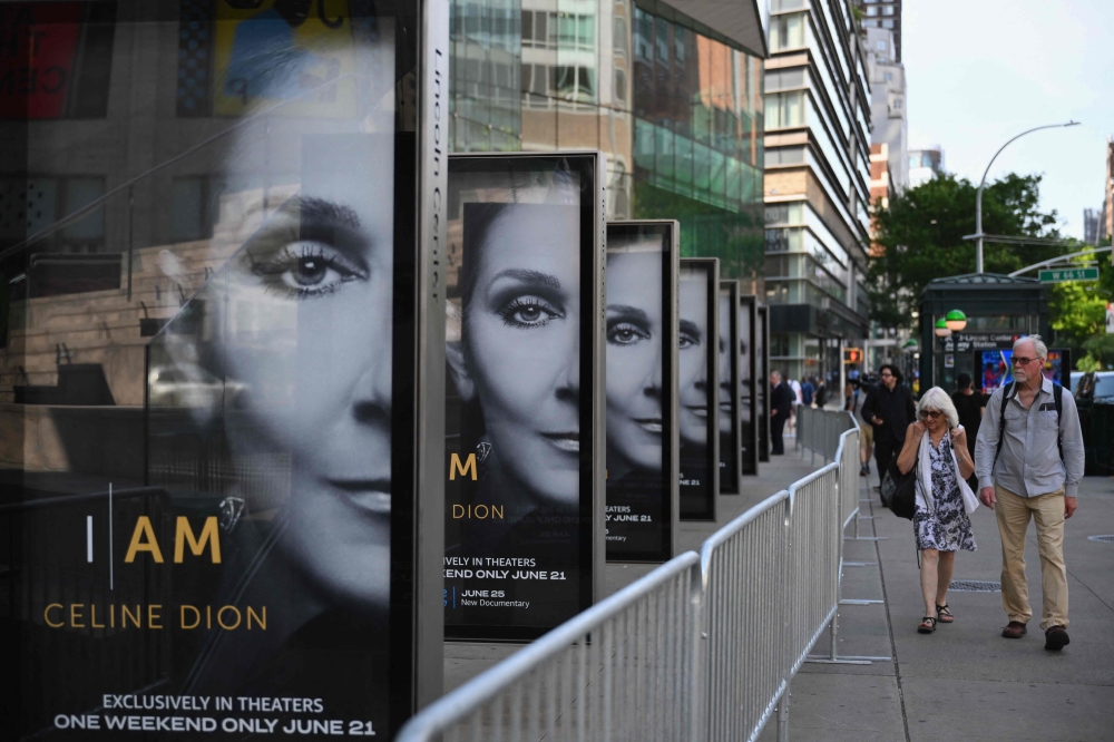 A person takes pictures of the "I Am: Celine Dion" digital billboards outside Alice Tully Hall in New York on Tuesday. — AFP 


