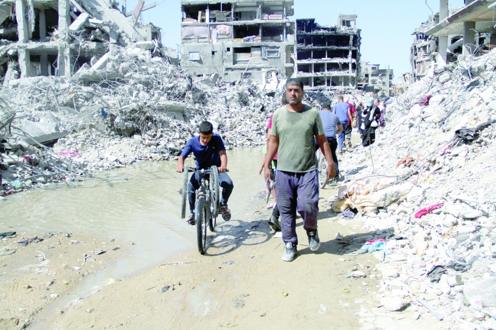 Palestinians walk near houses destroyed in the Israeli military offensive as they struggle with food scarcity, basic necessities, in Jabalia refugee camp. — Reuters 