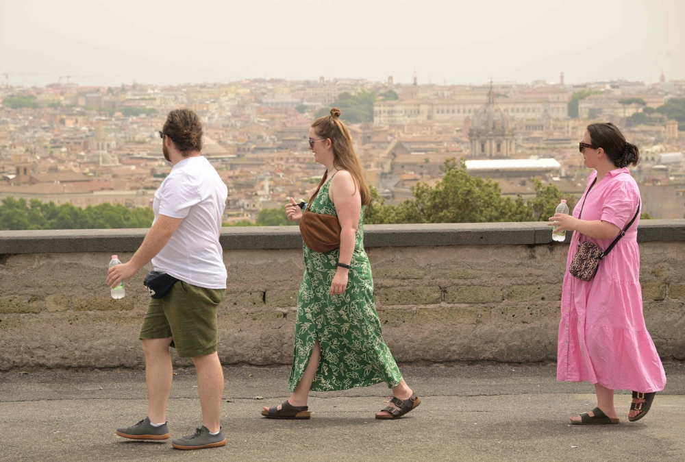 Tourists walk holding water bottles as a haze of heat is seen above Rome 
