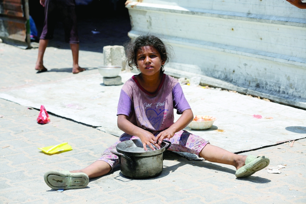 A girl sits as Palestinians gather to receive food cooked by a charity kitchen, amid shortages of aid supplies, in Khan Younis. — Reuters 