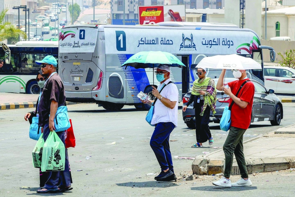 Departing pilgrims shade themselves with umbrellas as they walk past buses in Saudi Arabia's holy city of Mecca. - AFP