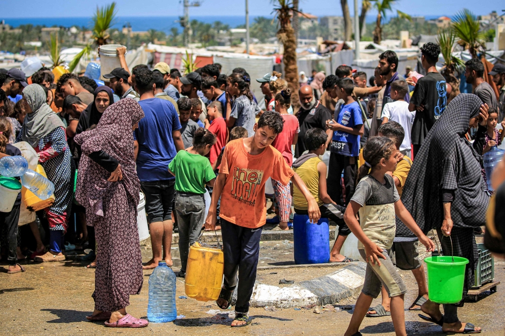 A boy walks with a jerrycan after filling up with others from a truck loaded with water cisterns in Rafah. — AFP 