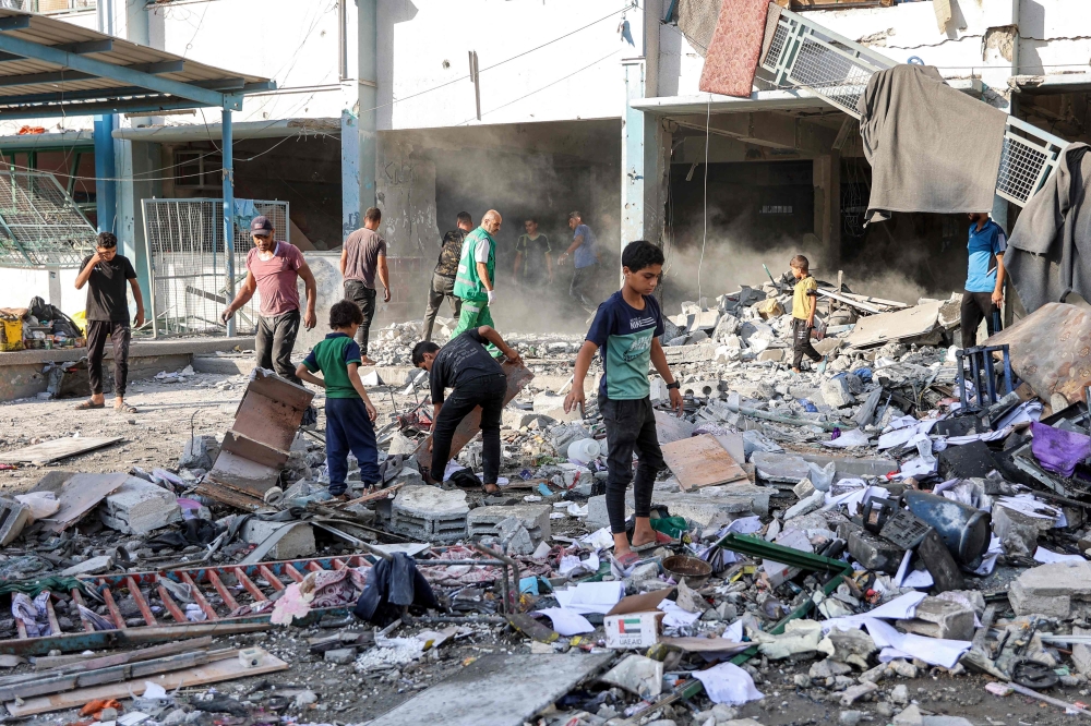 Men and children search through debris in the yard of the Asma school run by the UNRWA, in the Shati camp. — AFP 