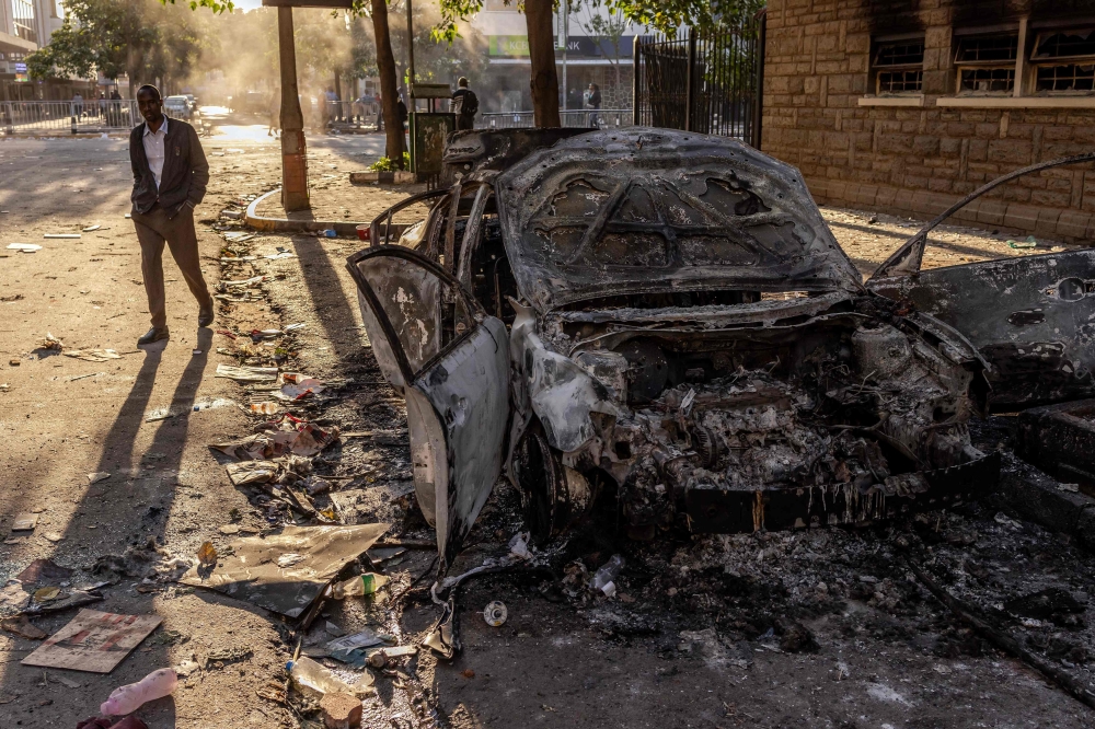 A man walks past the wreckage of a car burned down by protesters following a deadly nationwide strike to protest against tax hikes 
