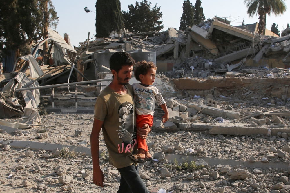 A Palestinian man carries a child while walking near rubble, following an Israeli strike on a school sheltering displaced people in Khan Younis, in the southern Gaza Strip. - Reuters

